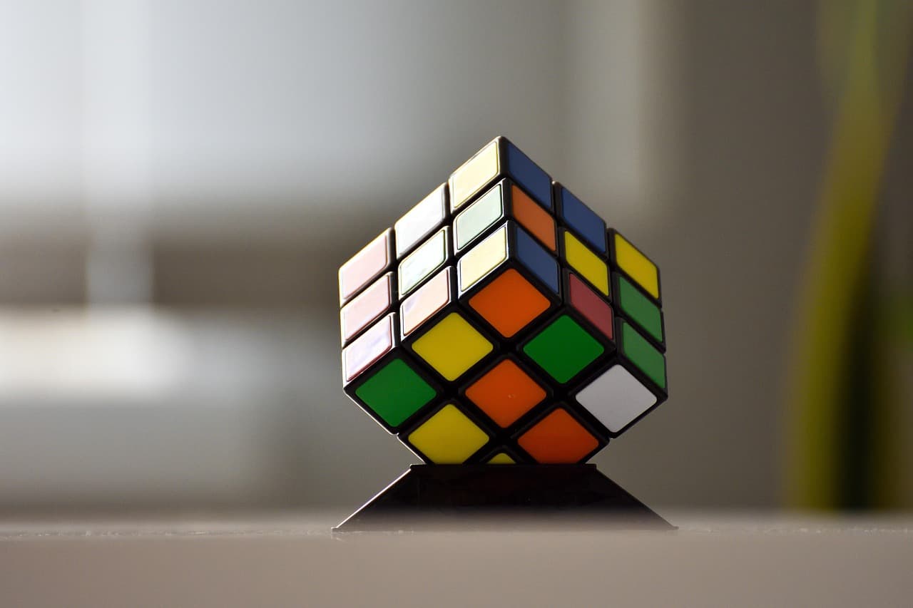A Rubix Cube being held up by a corner on a stand.